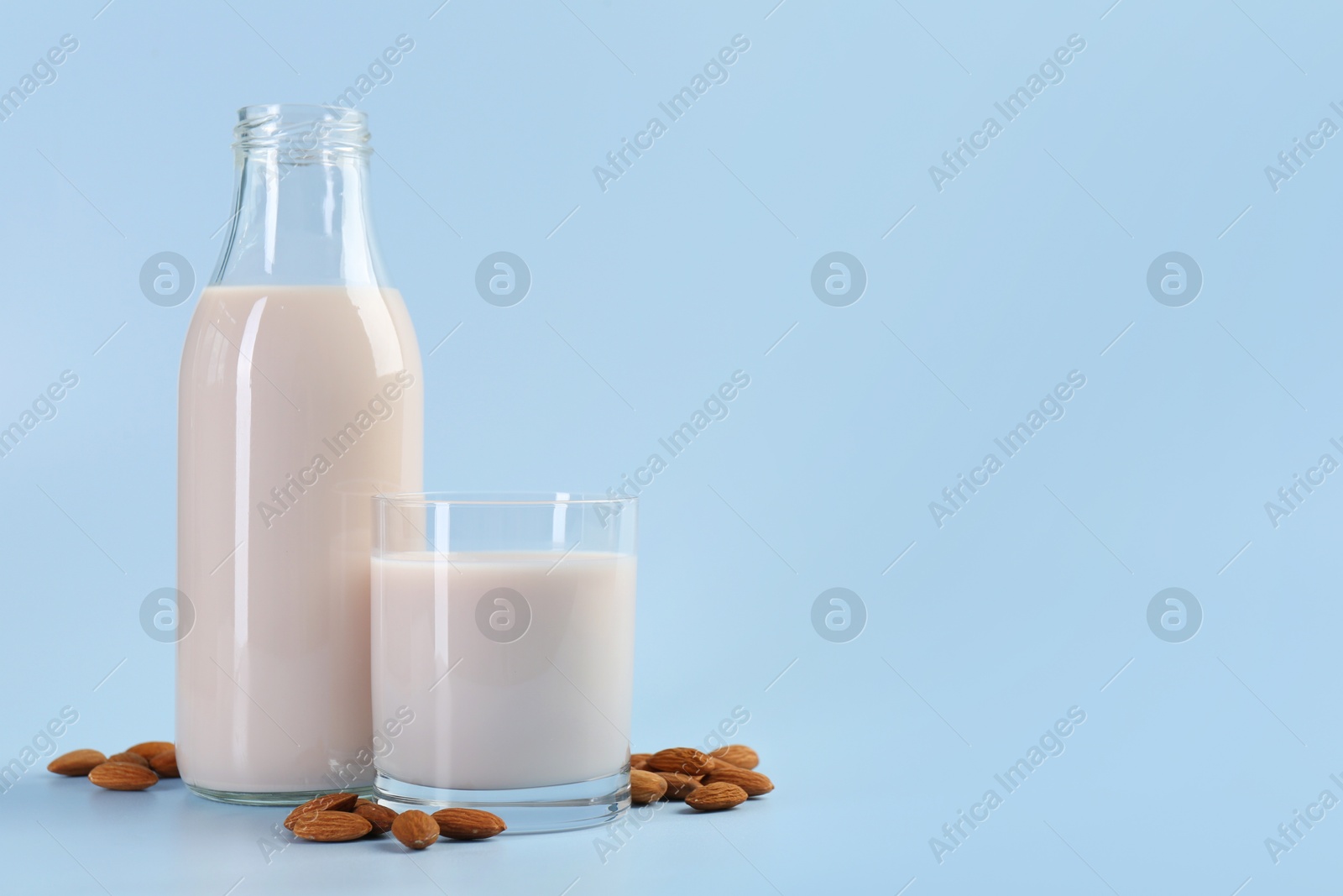 Photo of Fresh almond milk in bottle, glass and nuts on light blue background, space for text