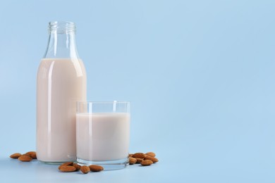 Photo of Fresh almond milk in bottle, glass and nuts on light blue background, space for text