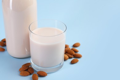 Photo of Fresh almond milk in glass, bottle and nuts on light blue background, space for text