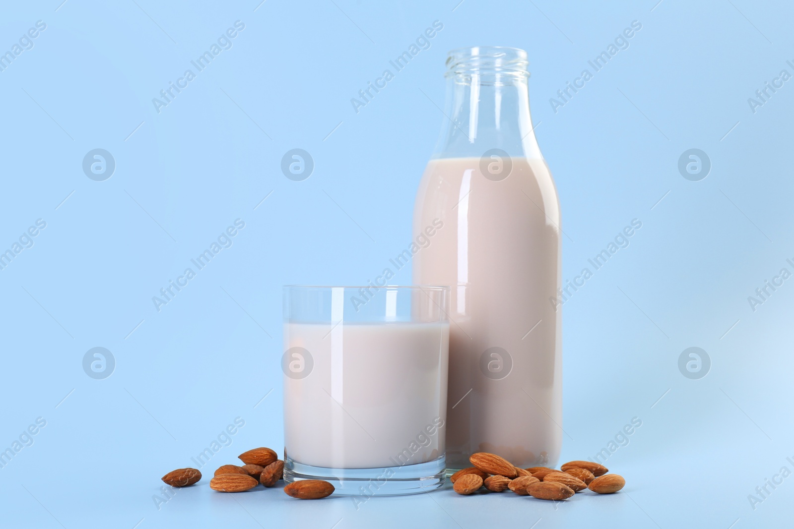 Photo of Fresh almond milk in bottle, glass and nuts on light blue background, space for text