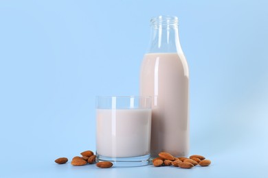 Photo of Fresh almond milk in bottle, glass and nuts on light blue background, space for text