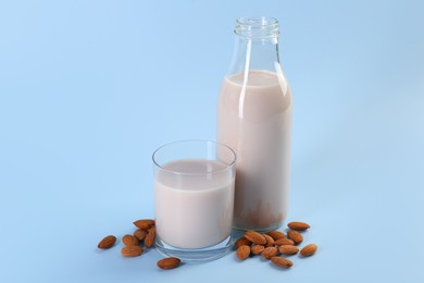 Photo of Fresh almond milk in bottle, glass and nuts on light blue background