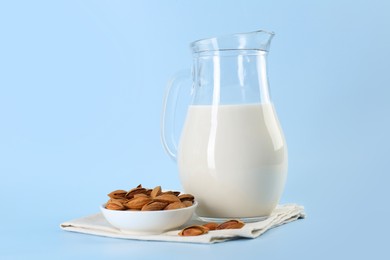 Photo of Fresh almond milk in glass jug and nuts on light blue background