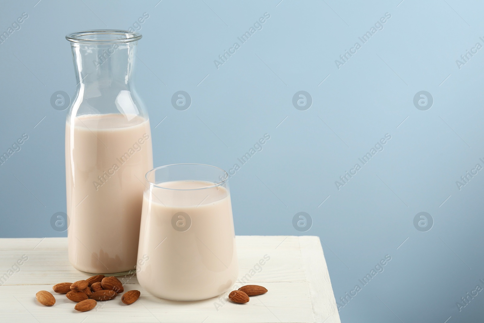 Photo of Fresh almond milk in carafe, glass and nuts on white wooden table, space for text