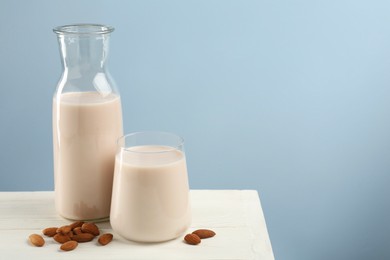 Photo of Fresh almond milk in carafe, glass and nuts on white wooden table, space for text