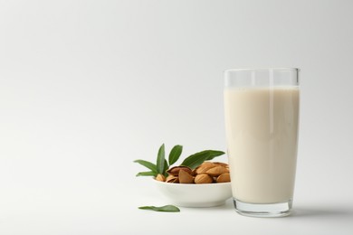 Photo of Fresh almond milk in glass, nuts and green leaves on white background, space for text