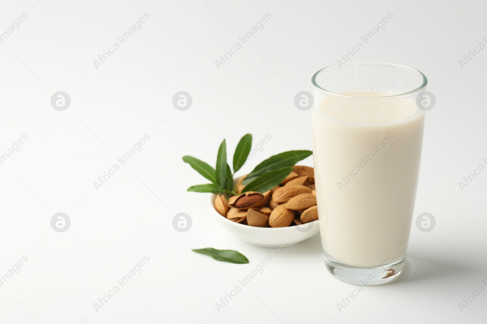 Photo of Fresh almond milk in glass, nuts and green leaves on white background, space for text