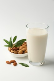 Fresh almond milk in glass, nuts and green leaves on white background