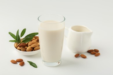 Photo of Fresh almond milk in glass, nuts, green leaves and pitcher on white background