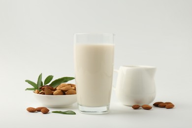 Photo of Fresh almond milk in glass, nuts, green leaves and pitcher on white background