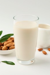 Photo of Fresh almond milk in glass, nuts and green leaves on white background