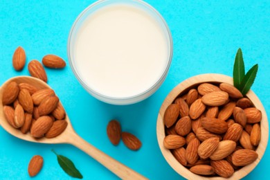 Photo of Fresh almond milk in glass, nuts, spoon and green leaves on light blue background, flat lay