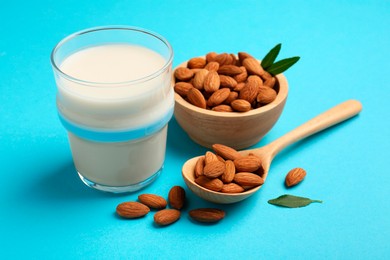 Fresh almond milk in glass, nuts, spoon and green leaves on light blue background