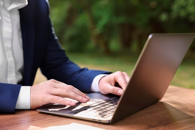 Photo of Businessman working with laptop at table outdoors, closeup. Remote job