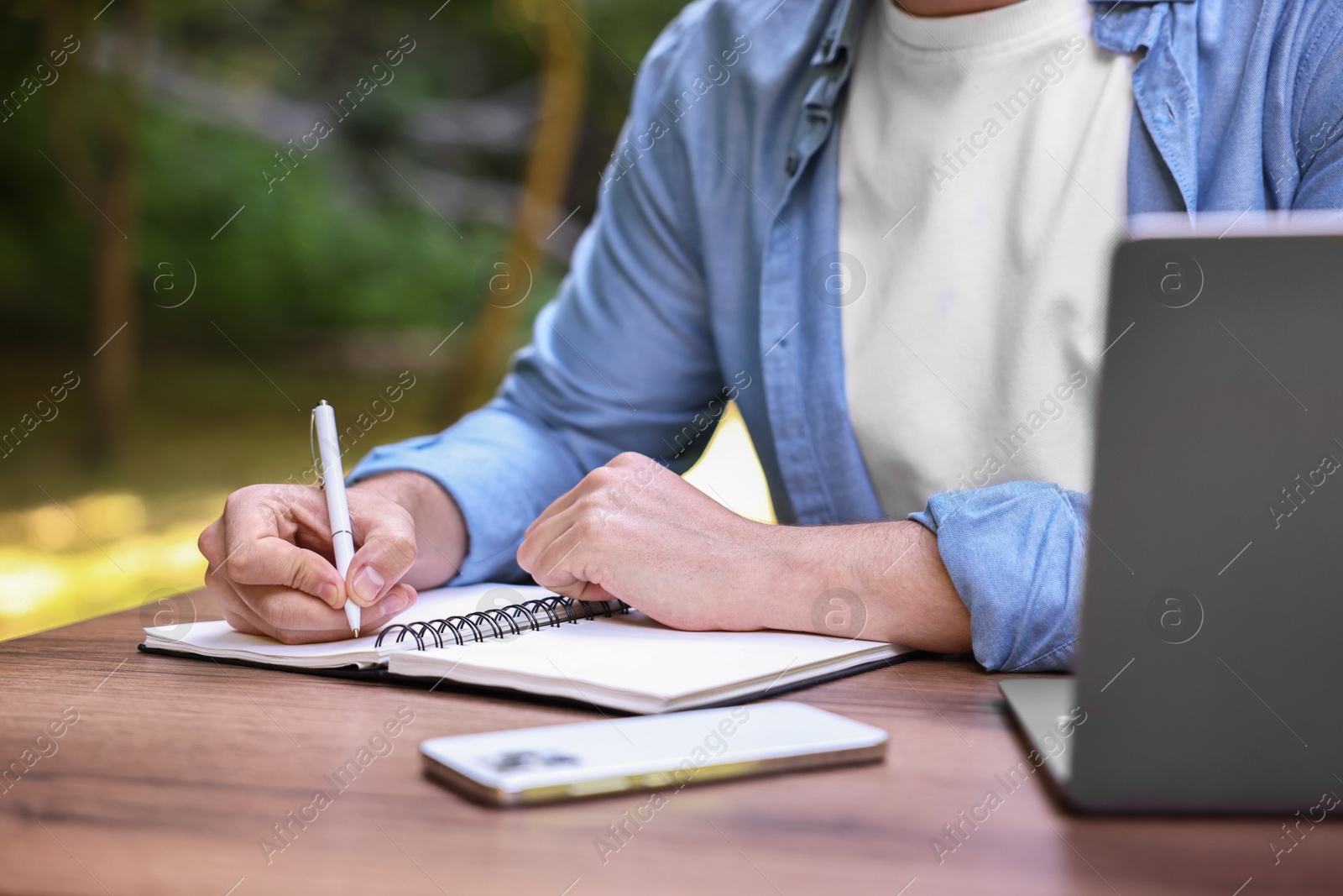 Photo of Freelancer writing something at table outdoors, closeup. Remote job