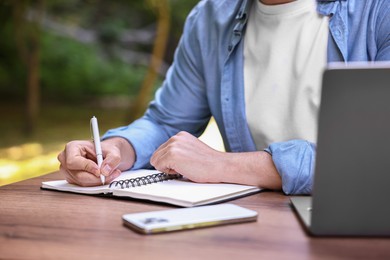 Freelancer writing something at table outdoors, closeup. Remote job