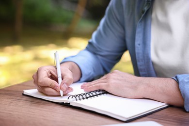 Photo of Freelancer writing something at table outdoors, closeup