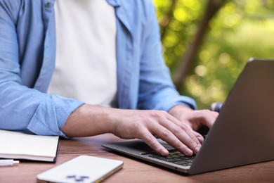 Photo of Freelancer working with laptop at table outdoors, closeup. Remote job