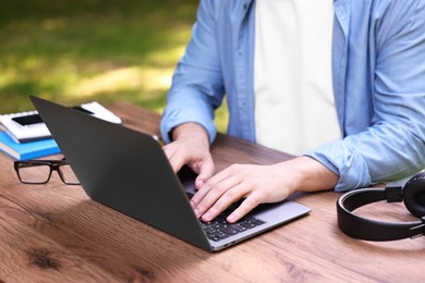 Photo of Freelancer working with laptop at wooden table outdoors, closeup. Remote job