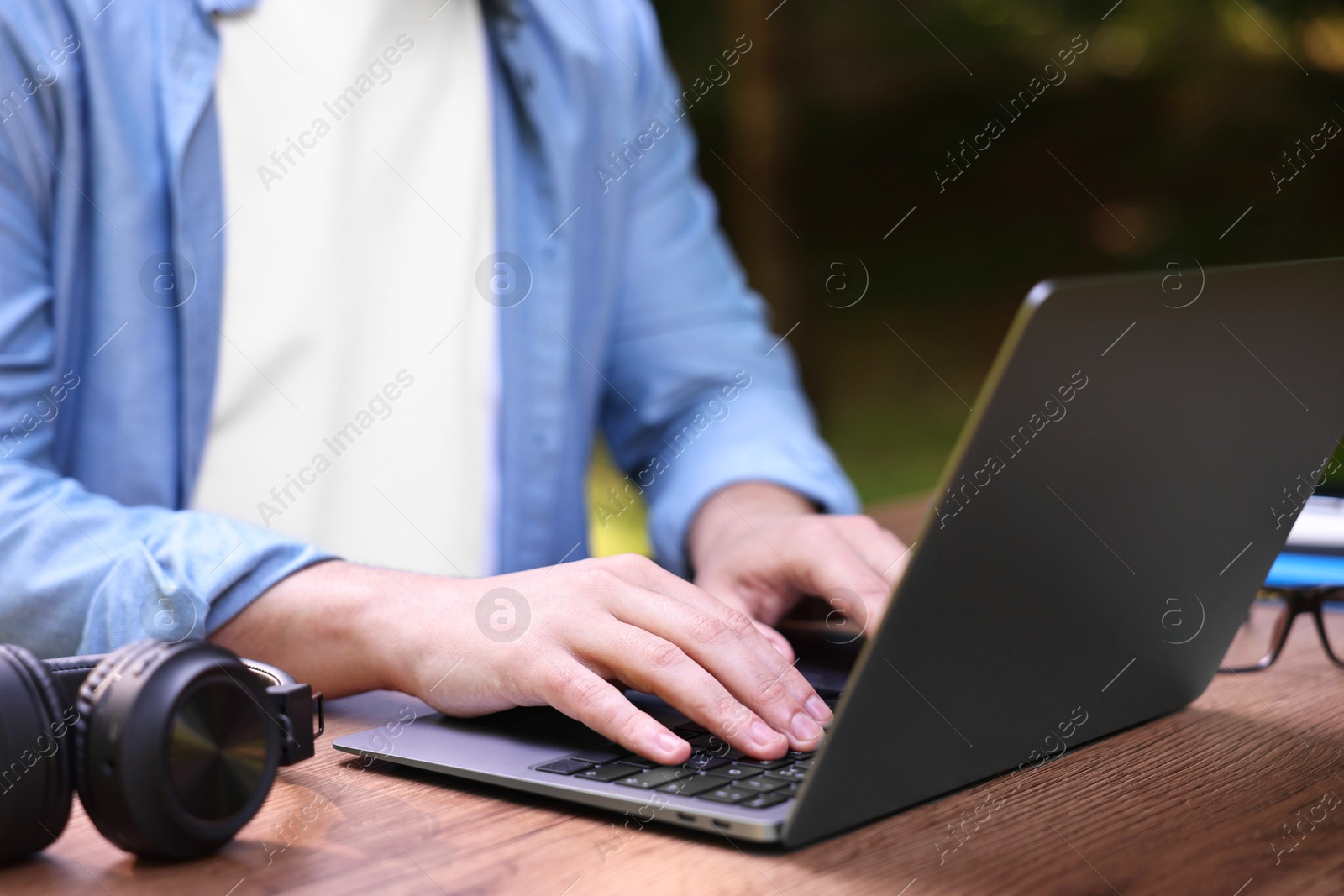 Photo of Freelancer working with laptop at wooden table outdoors, closeup. Remote job