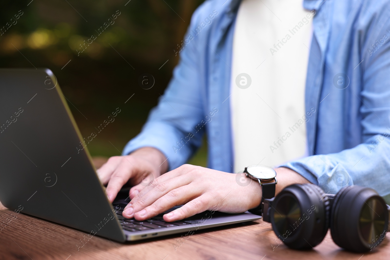 Photo of Freelancer working with laptop at wooden table outdoors, closeup. Remote job