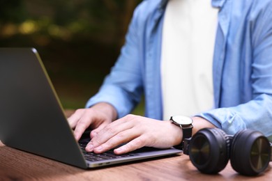 Photo of Freelancer working with laptop at wooden table outdoors, closeup. Remote job