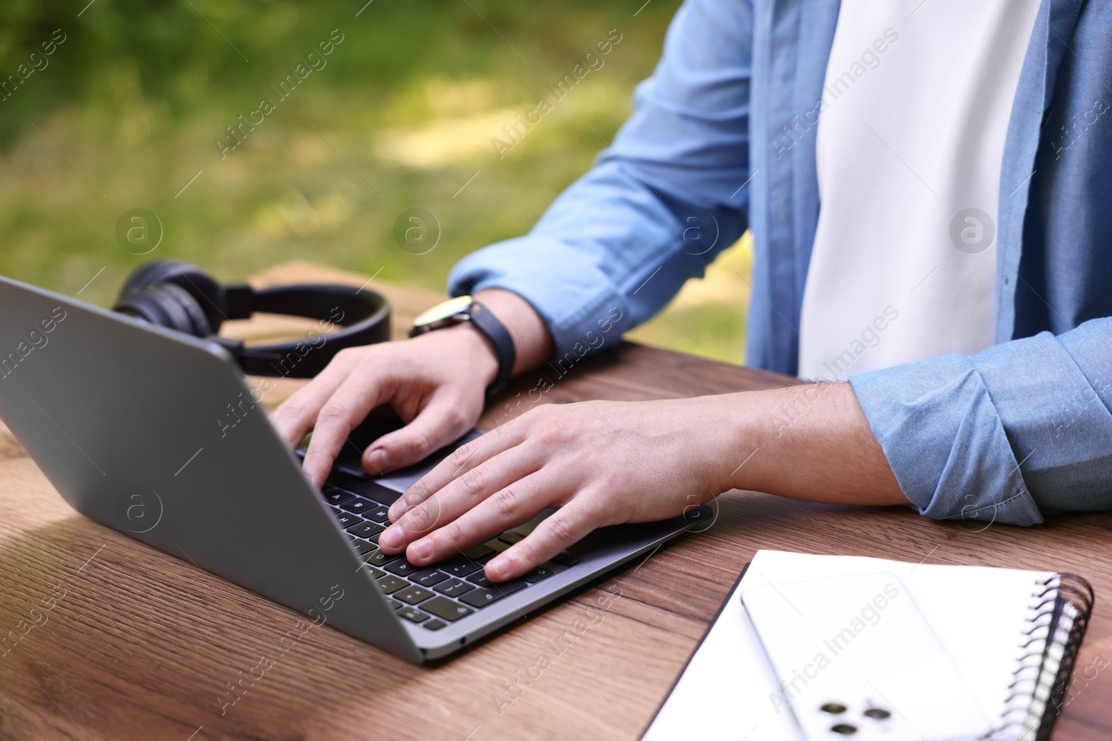 Photo of Freelancer working with laptop at wooden table outdoors, closeup. Remote job