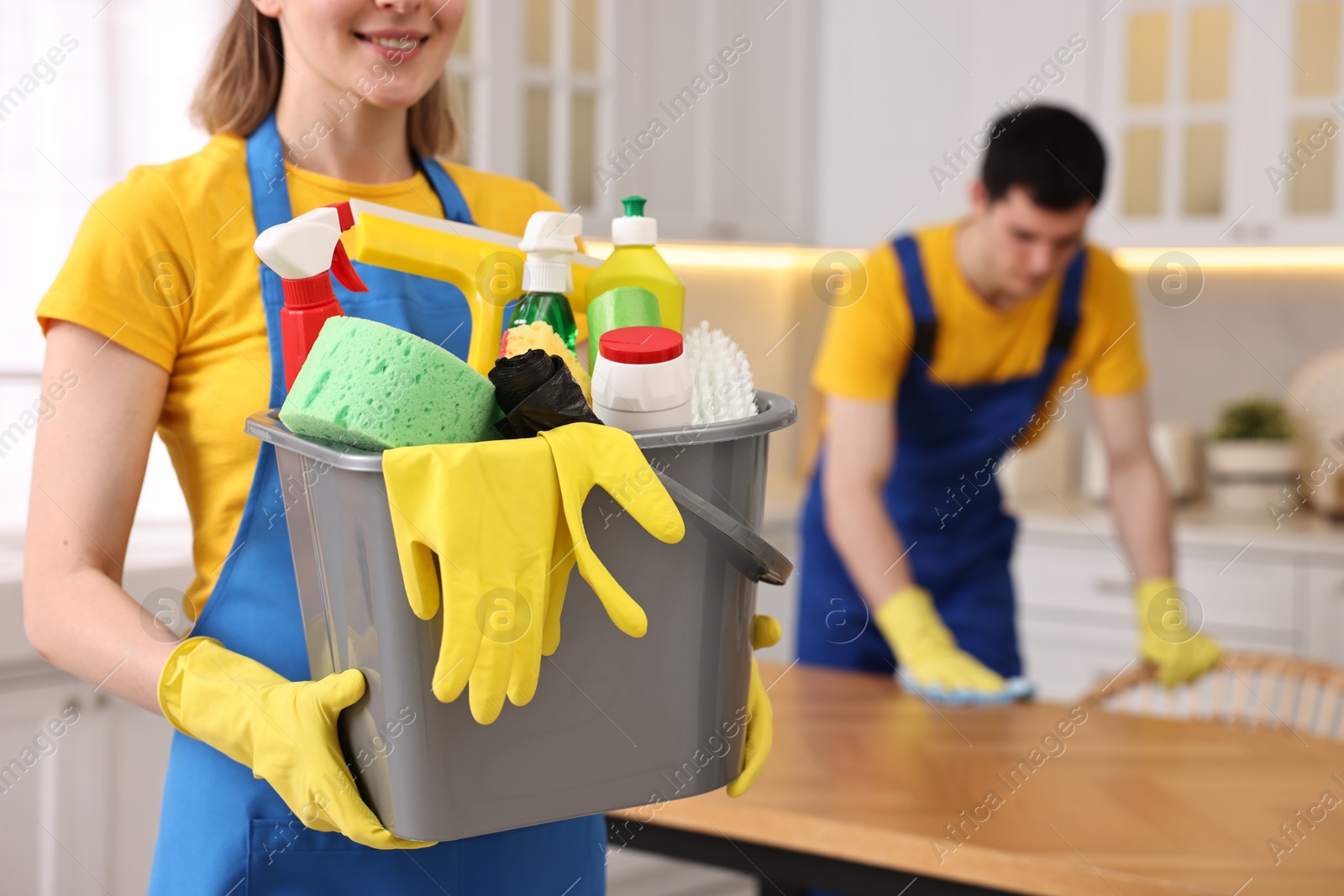 Photo of Cleaning service worker holding bucket with supplies in kitchen, closeup