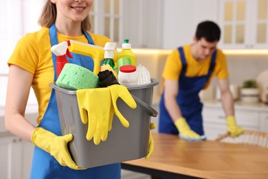 Photo of Cleaning service worker holding bucket with supplies in kitchen, closeup