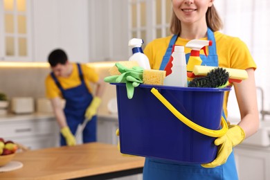 Photo of Cleaning service worker holding bucket with supplies in kitchen, closeup