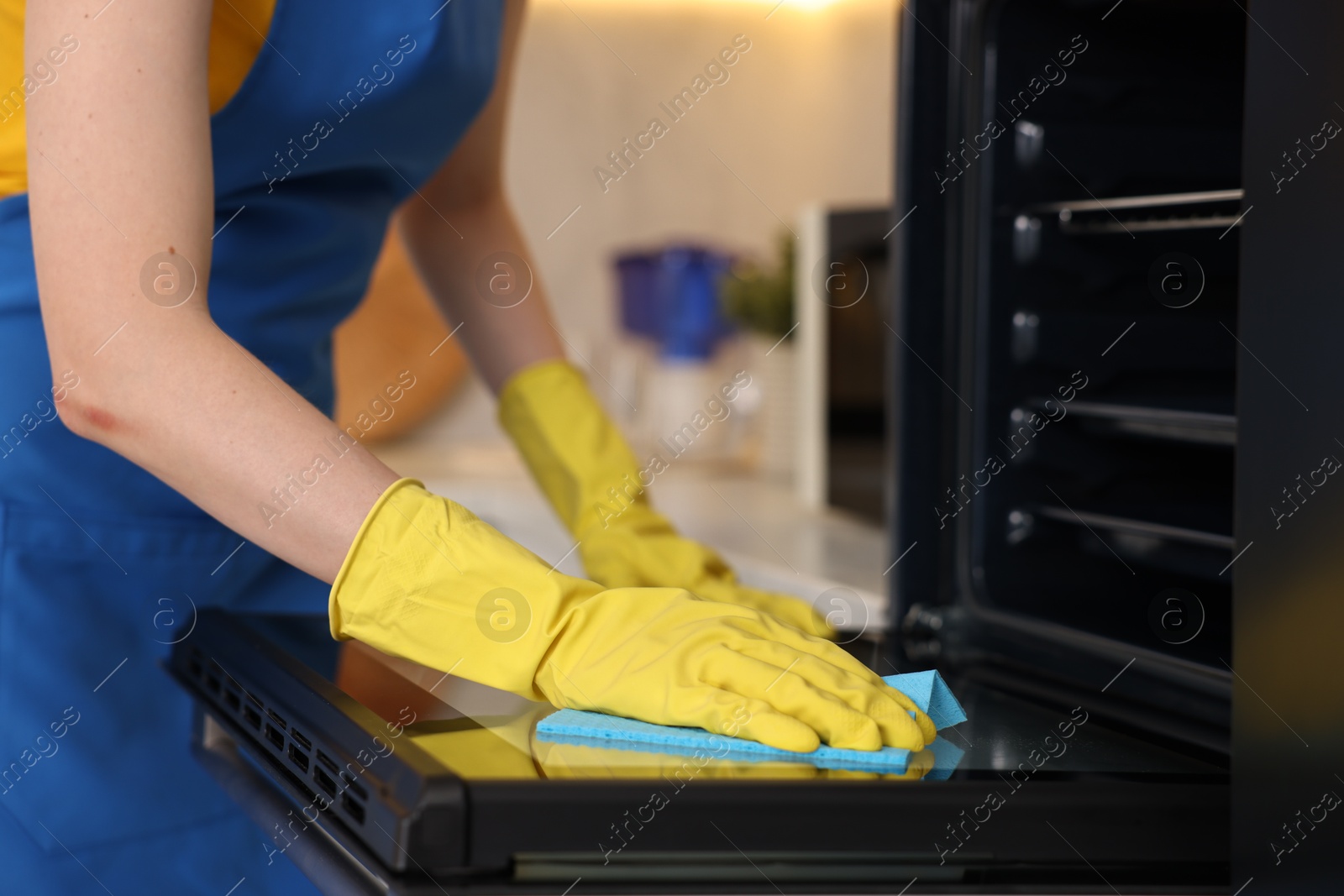 Photo of Professional janitor wearing uniform cleaning electric oven in kitchen, closeup