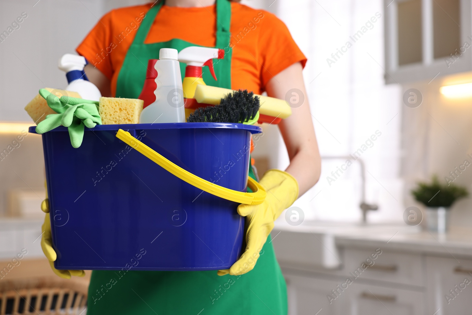 Photo of Cleaning service worker holding bucket with supplies in kitchen, closeup