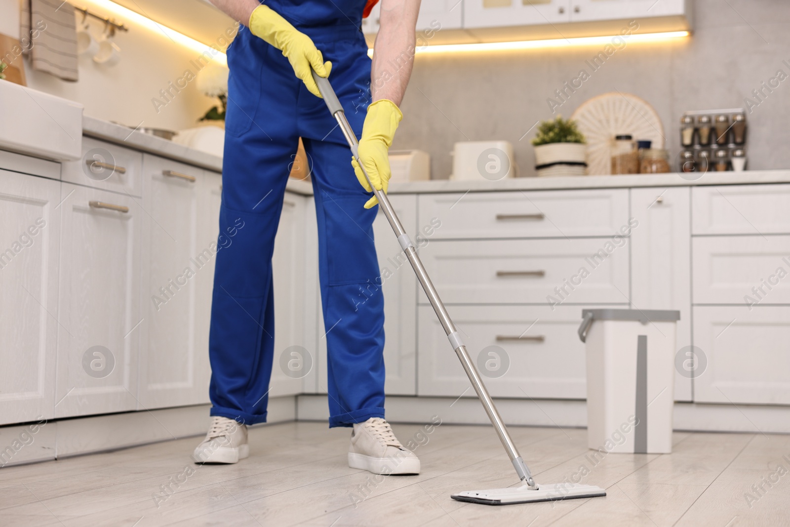 Photo of Cleaning service worker washing floor with mop in kitchen, closeup