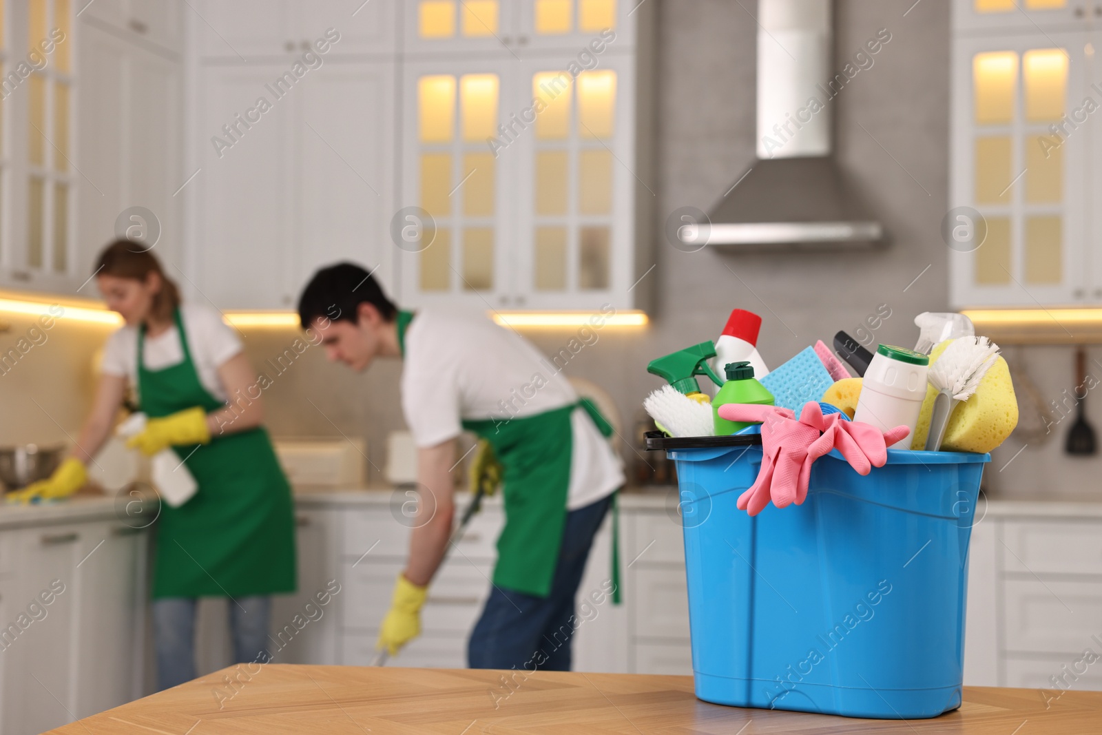 Photo of Professional janitors working in kitchen, focus on bucket with supplies. Cleaning service