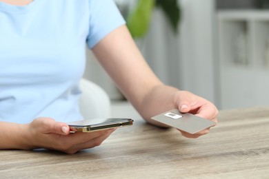 Photo of Woman holding SIM card and smartphone at wooden table indoors, closeup