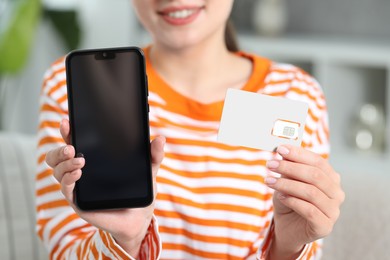 Photo of Woman holding SIM card and smartphone indoors, closeup