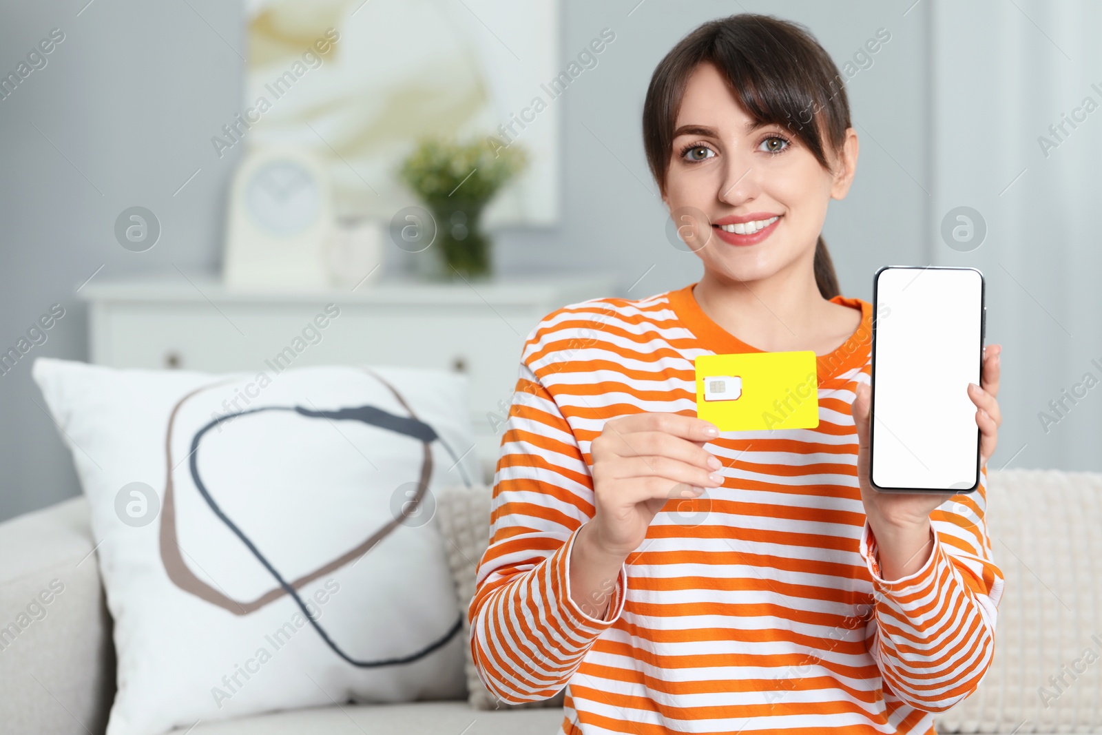 Photo of Woman holding SIM card and smartphone on sofa indoors