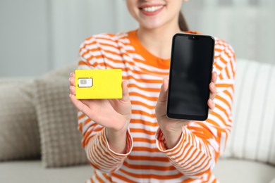 Photo of Woman holding SIM card and smartphone on sofa indoors, closeup