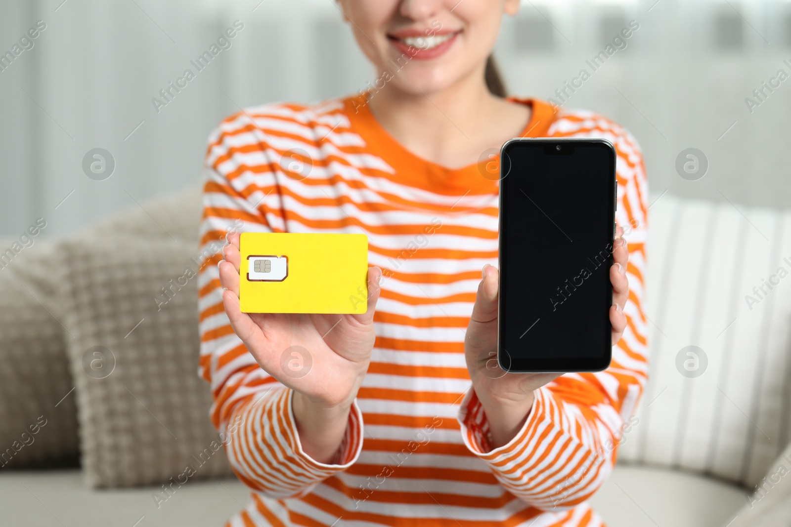 Photo of Woman holding SIM card and smartphone on sofa indoors, closeup