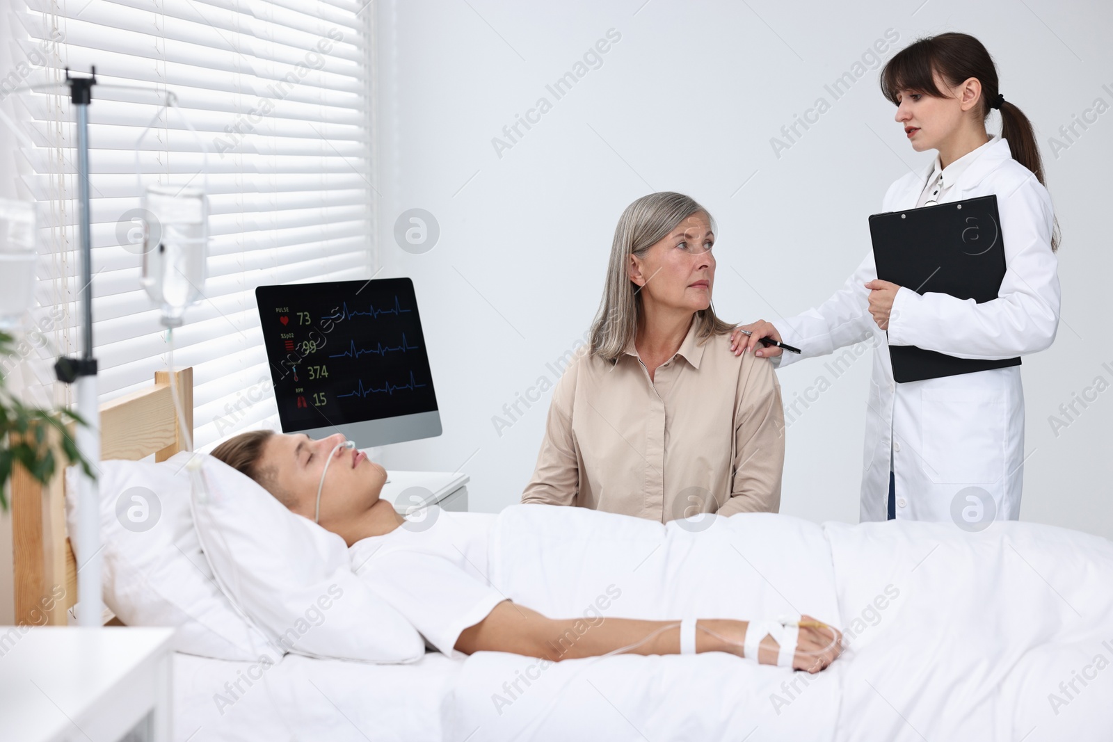 Photo of Coma patient. Sad mature woman near her unconscious son talking with doctor in hospital