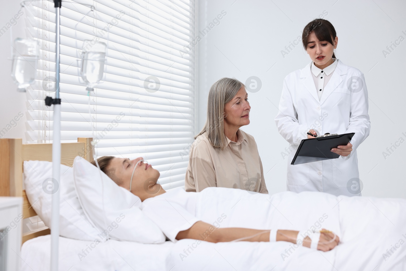 Photo of Coma patient. Sad mature woman near her unconscious son talking with doctor in hospital