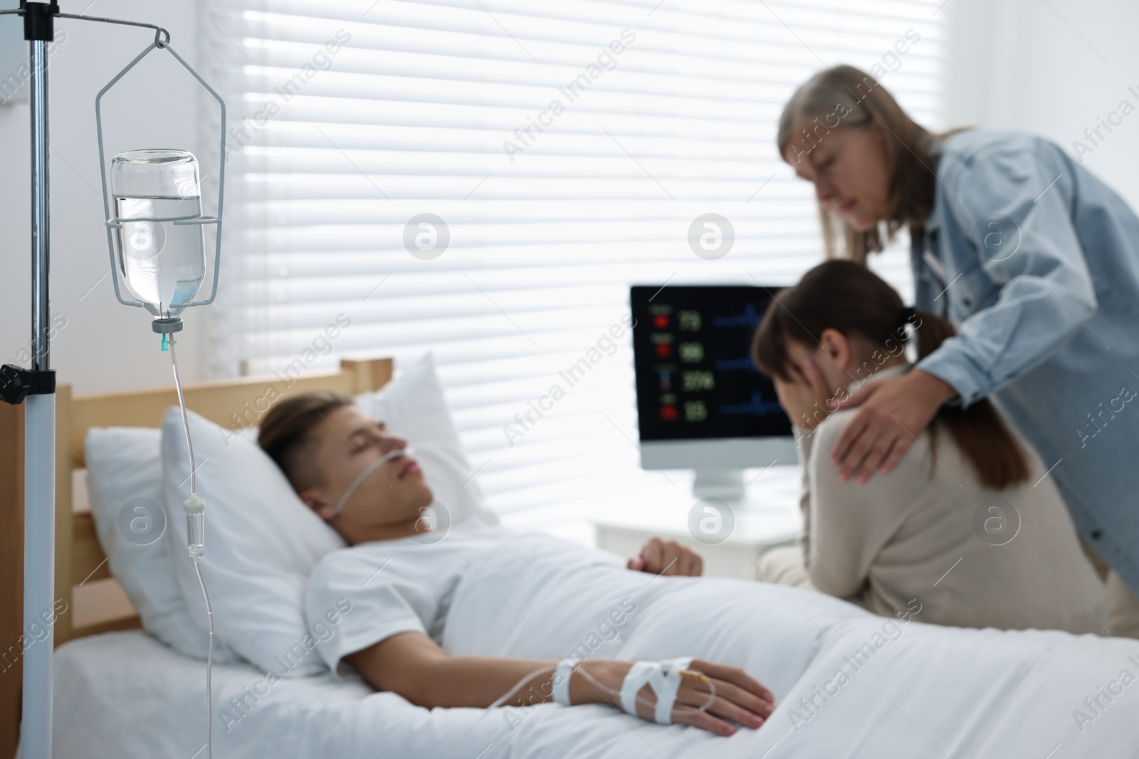 Photo of Coma patient. Sad women near unconscious young man in hospital