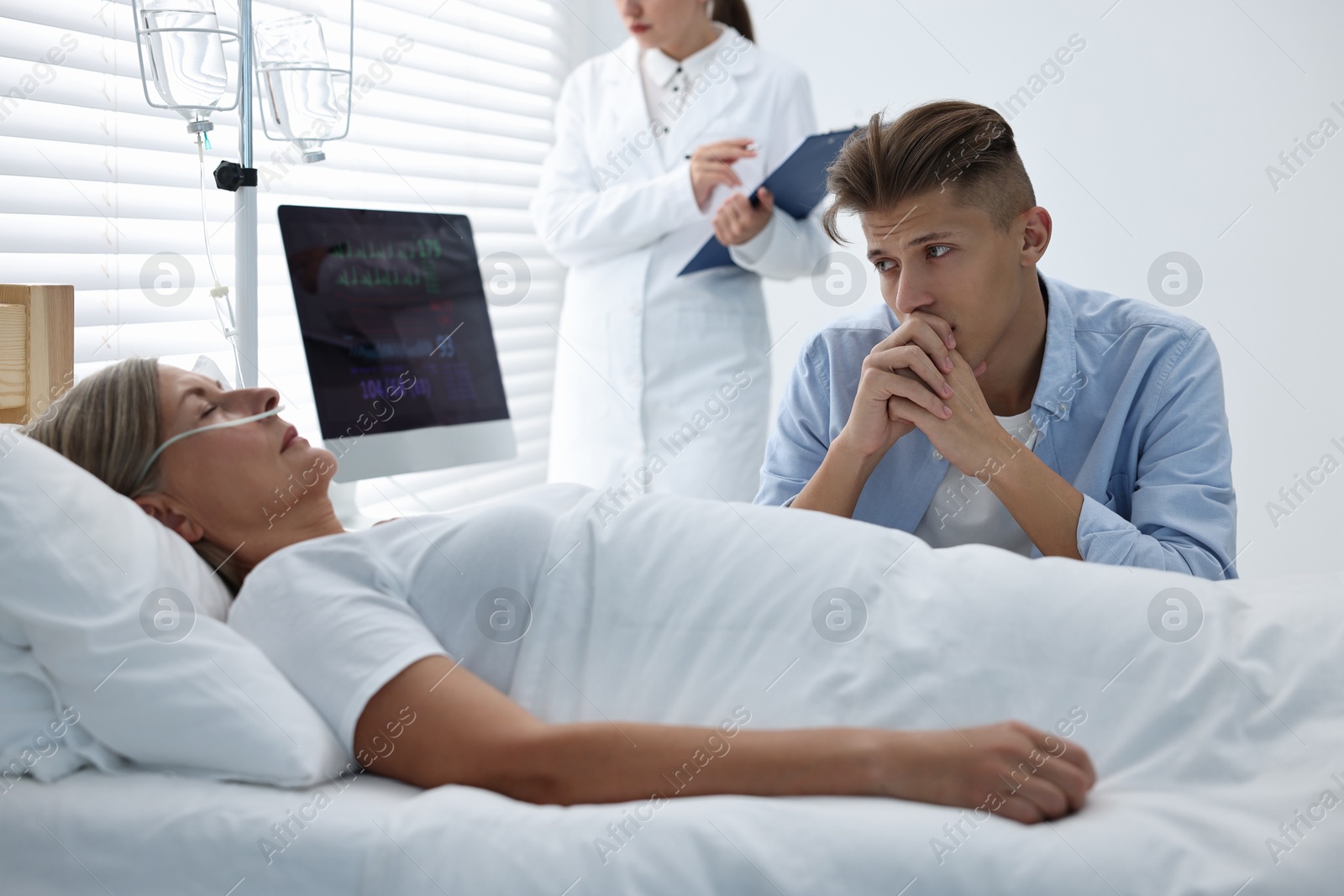 Photo of Coma patient. Sad young man near his unconscious mother in hospital