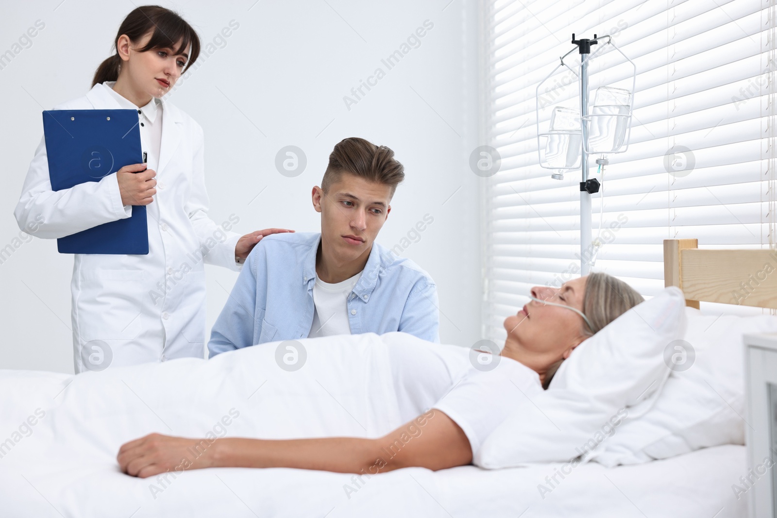 Photo of Coma patient. Sad young man near his unconscious mother talking with doctor in hospital