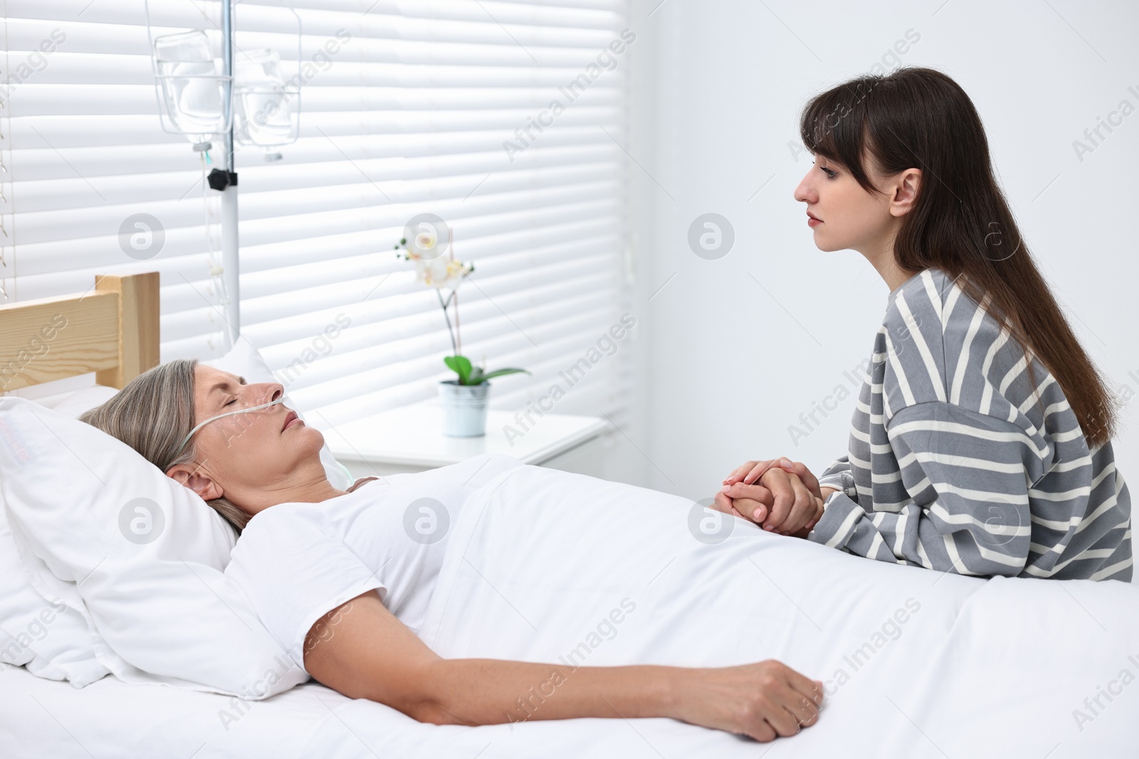 Photo of Coma patient. Sad young woman near her unconscious mother in hospital