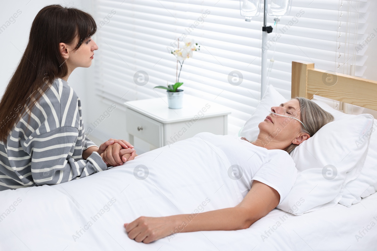 Photo of Coma patient. Sad young woman near her unconscious mother in hospital