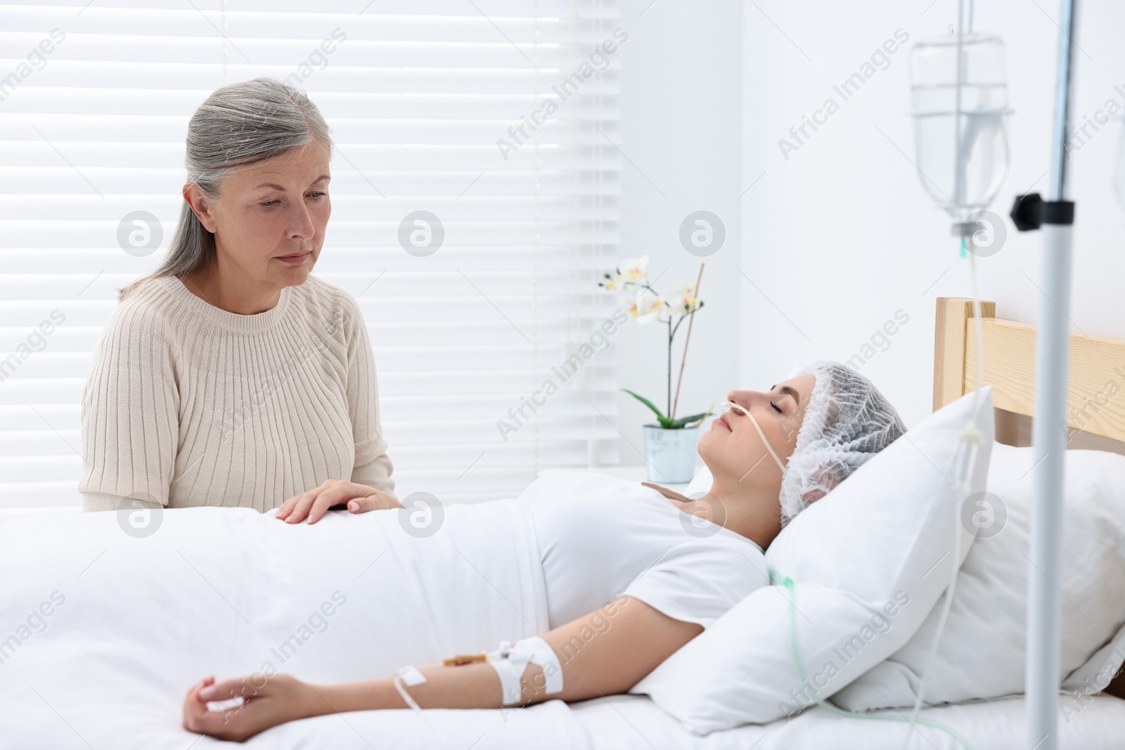 Photo of Coma patient. Sad mature woman near her unconscious daughter in hospital