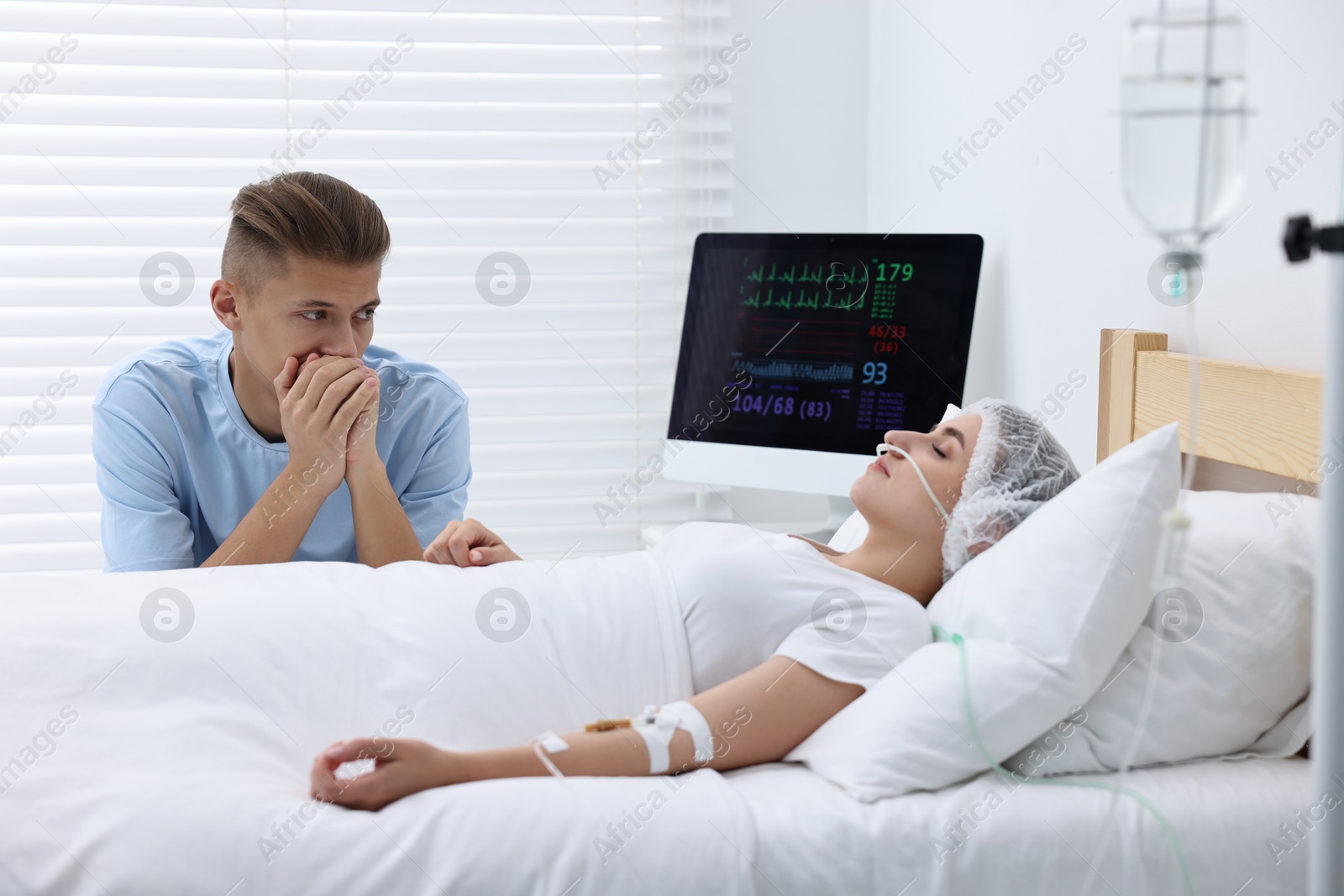 Photo of Coma patient. Sad young man near his unconscious wife in hospital