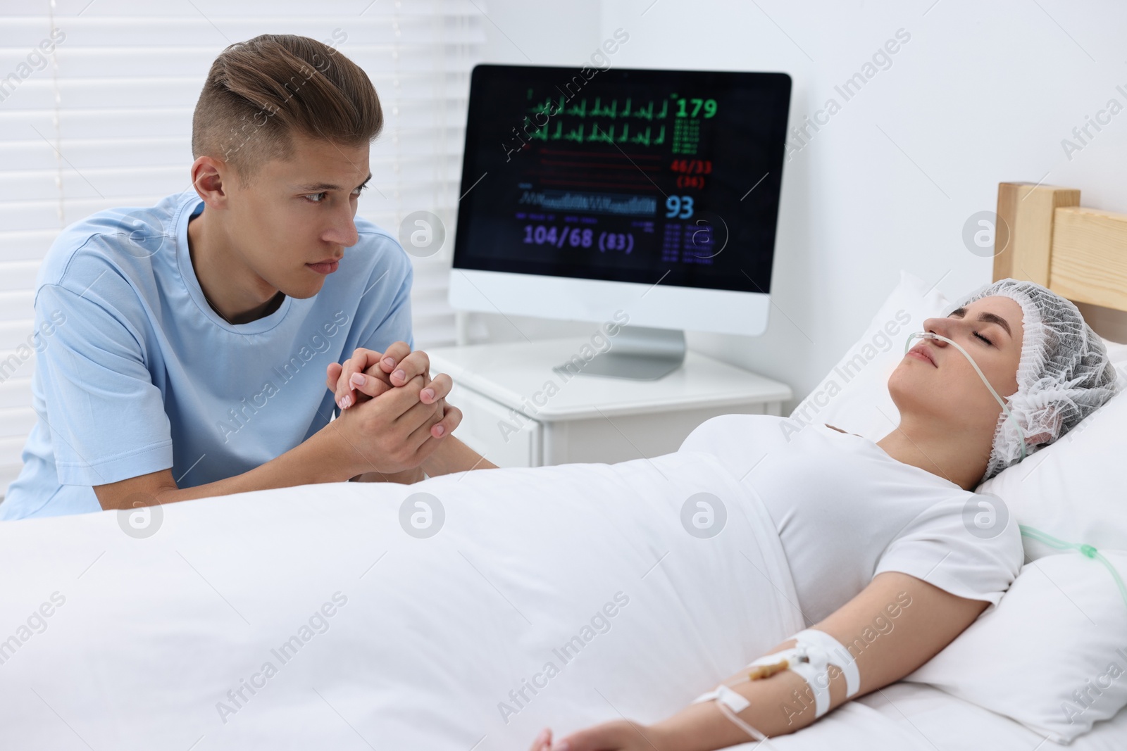 Photo of Coma patient. Sad young man near his unconscious wife in hospital