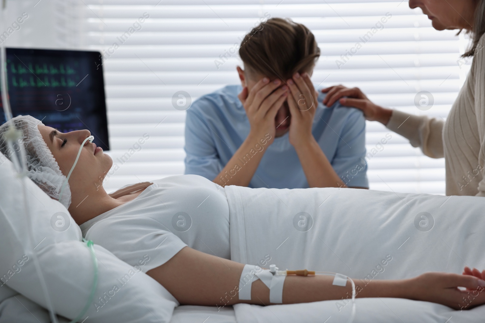 Photo of Coma patient. Sad relatives near sleeping young woman in hospital